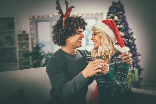 Young romantic couple hugging and celebrating Christmas at home, they are having fun and toasting with beer. Selective focus.