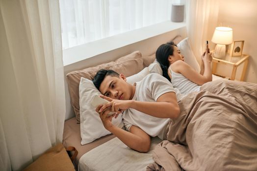 Young couple with smartphones in their bed