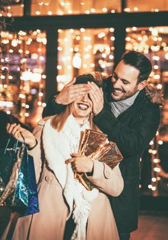 Young man covering the eyes of happy surprised girlfriend in Christmas night.
