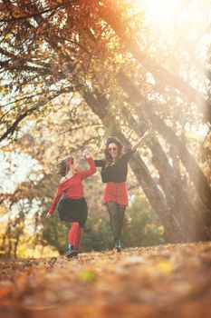 Beautiful young mother and her happy daughter having fun in the forest in sunset. They are holding hands, laughing and jumping.