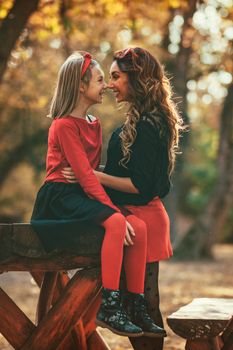 Beautiful young mother and her happy daughter having fun in the forest in sunset. They are hugging, smiling and looking each other.