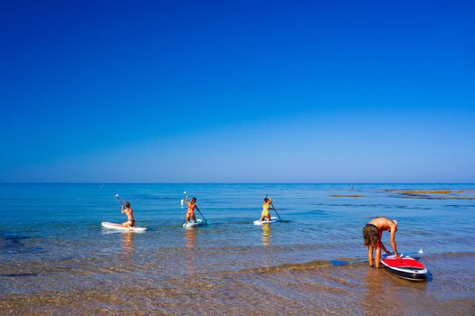 Stand up paddle boarding. Joyful group of friendsare training SUP board in the mediterranean sea on a sunny morning in Realmonte beach, Sicily. Italy