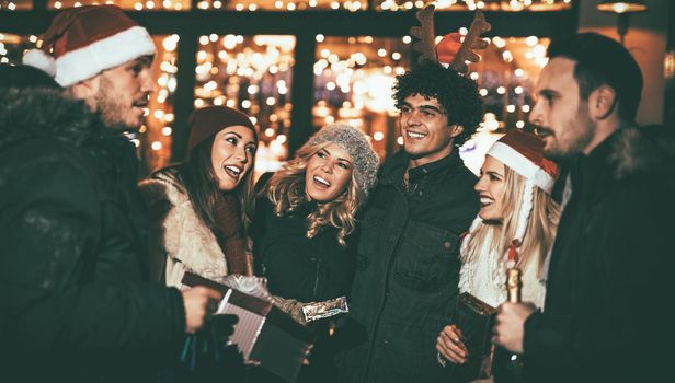 Three young cheerful couple having fun at the Christmas outdoor party in the city street at night and with a lot of lights on background.