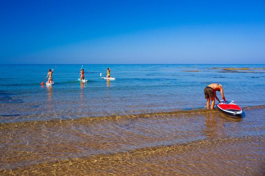 Stand up paddle boarding. Joyful group of friendsare training SUP board in the mediterranean sea on a sunny morning in Realmonte beach, Sicily. Italy