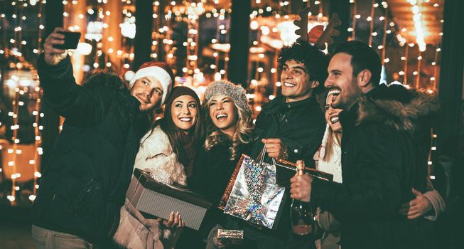 Young beautiful cheerful friends taking a selfie in the city street at new year's night with a lot of lights on background. 