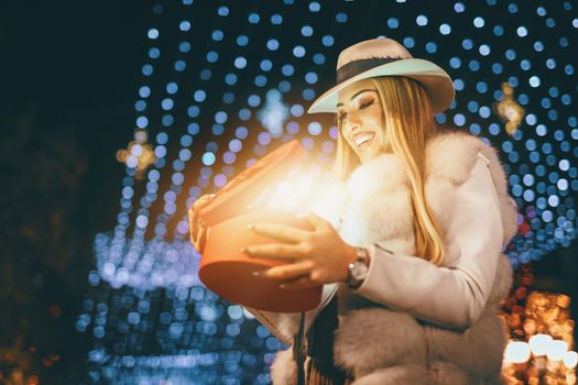 Cheerful young woman with red present having fun in the city street at Christmas time.