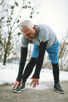 Active senior man stretching and doing exercises in public park during the winter training outside in.