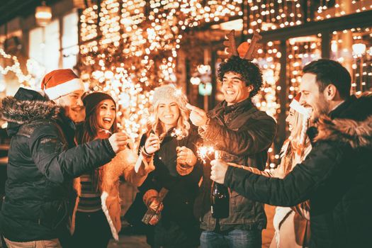 Group of happy friends having fun with sparklers on night Christmas party.