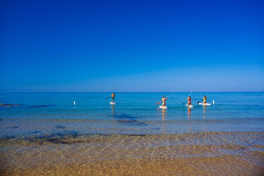 Stand up paddle boarding. Joyful group of friendsare training SUP board in the mediterranean sea on a sunny morning in Realmonte beach, Sicily. Italy