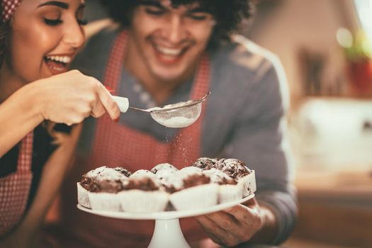 Happy loving couple is sprinkling powdered sugar on roasted chocolade muffin.
