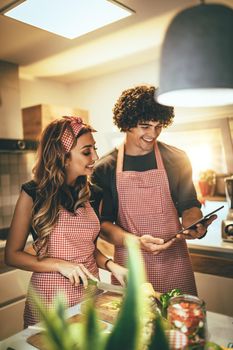 Young happy couple is enjoying and preparing healthy meal in their kitchen and reading recipes on the tablet.