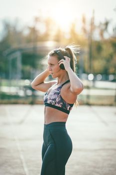 Beautiful young woman runner athlete putting her earphones during preparing to run.