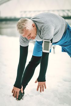 Active senior man stretching and doing exercises by the river during the winter training outside in.