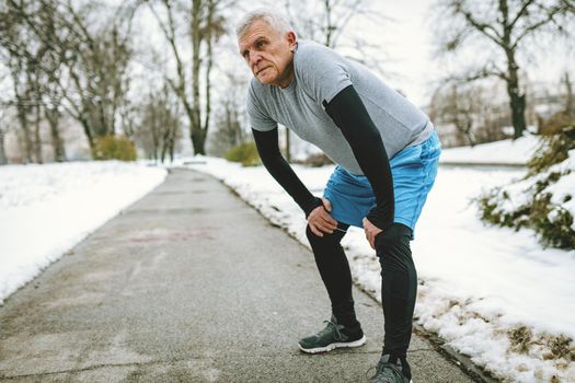 Active senior making pause during jogging and  doing exercises in public park during the winter training outside in. Copy space.