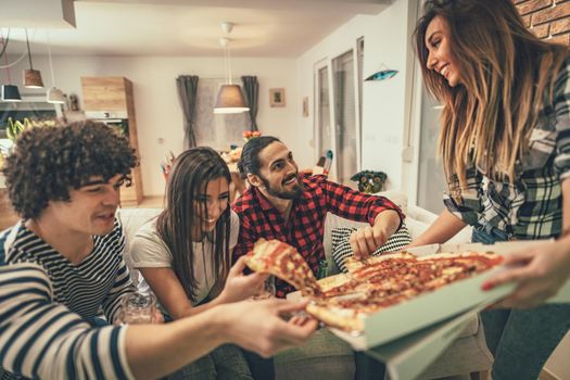 Excited friends is at home sitting on sofa. Their friends bring pizza to eat together. They have great weekend in nice company indoors. 