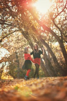 Beautiful young mother and her happy daughter having fun in the forest in sunset. They are holding hands, laughing and jumping.