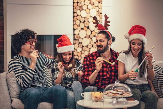 Cute beautiful couple is spending New Year eve at home sitting on sofa and have a great holidays having fun in nice company indoors. 