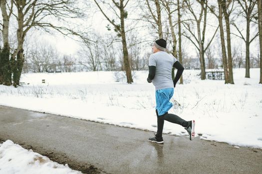 Active senior man running and doing exercises in public park during the winter training outside in. Copy space.