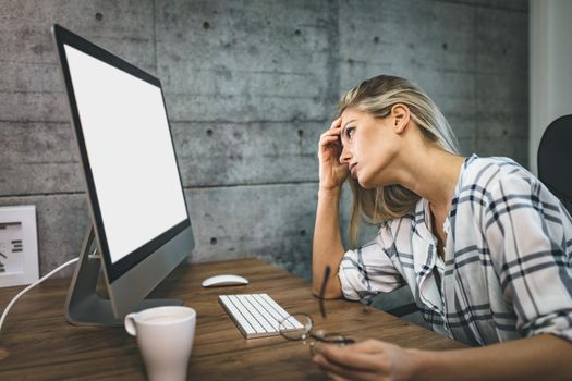 Young handsome frustrated and stressed business woman sitting at the office front a computer and holding head.