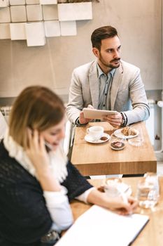 Beautiful young pensive man is checking social media at digital tablet and drinking coffee in a cafe. 