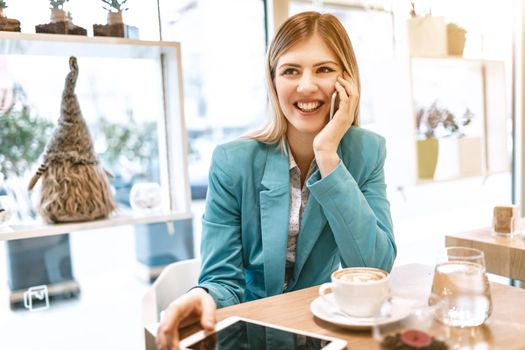 Young smiling businesswoman on a break in a cafe. He is drinking coffee and using smartphone. 