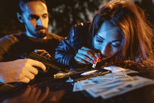 A criminal young woman drug addict sniffs a cocaine track with a rolled-up note. 