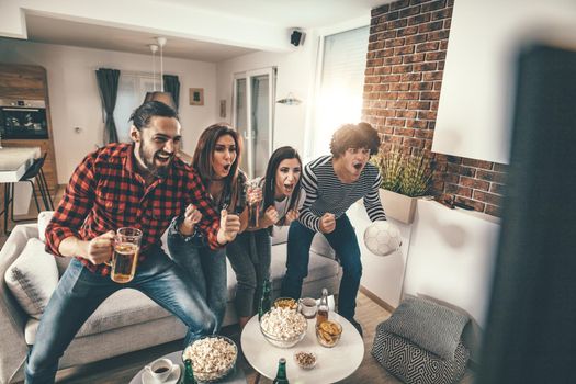 Friends are fans of sports games as football love spending their free time at home together. They are screaming and gesturing for a victory. 