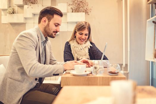 Two young smiling business people talking and working on laptop on a break at cafe.