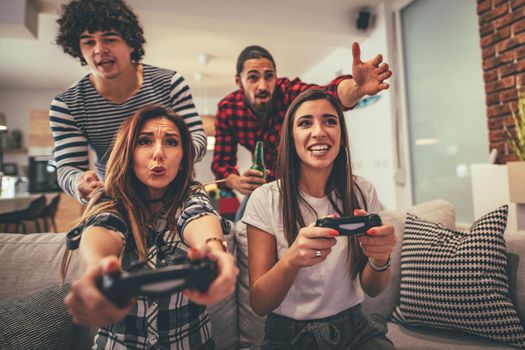 Excited two couple are playing video games at home sitting on sofa with beer. They have great weekend in nice company indoors. 