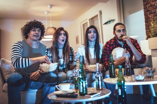 Friends are fans of sports games as football love spending their free time at home together. They are screaming and gesturing for a victory. 