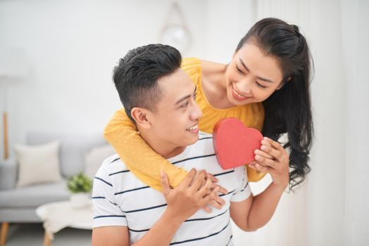 A asian couple sitting on couch give a red gift box for present in a special day