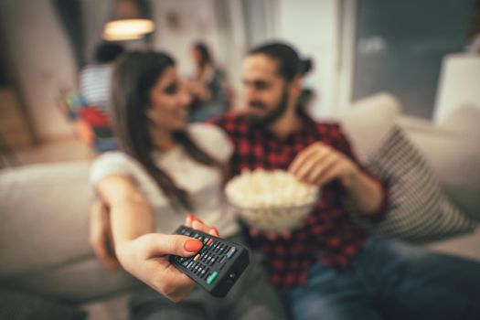 Excited couple is looking movie on TV at home sitting on sofa with popcorn. They have great weekend in nice company indoors. 