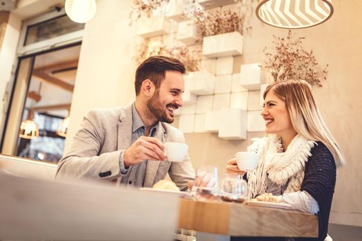 Young man and young woman sitting at cafe and talking with smile. They drinking coffee and having breakfast.