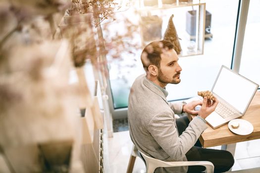 Young businessman on a break in a cafe. He is working at laptop and using having breakfast. 