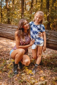 Beautiful young mother and her daughter walking through autumn forest.