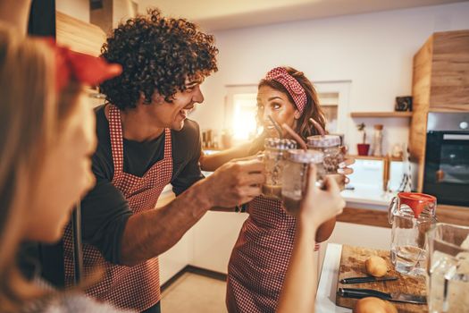 Young smiling family is toasting with fruit smoothie in the kitchen.