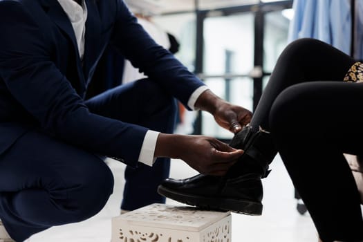 Retail employee helping african american client with purchase in shopping center. Stylish customer trying stylish shoes, buying trendy merchandise in boutique, commercial activity. Close up