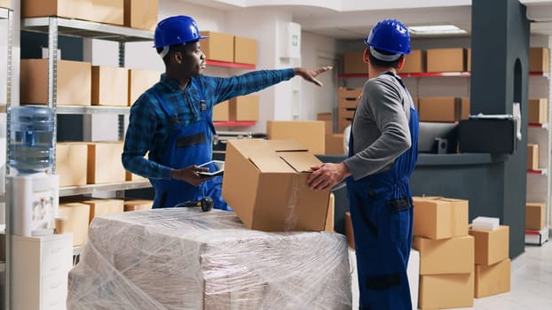 Team of diverse men looking at boxes of products in storage room, scanning barcodes to check stock logistics for distribution. Employee and supervisor in overalls working with goods.