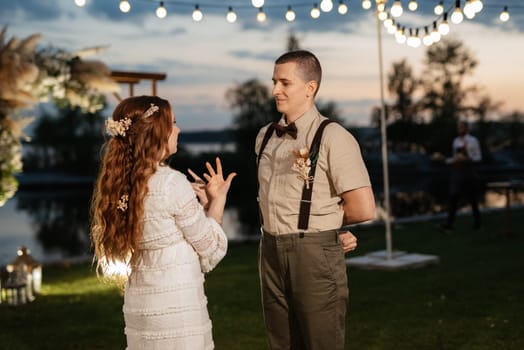 the first wedding dance of the bride and groom in the glade of the country club in the light of sunset and warm garlands