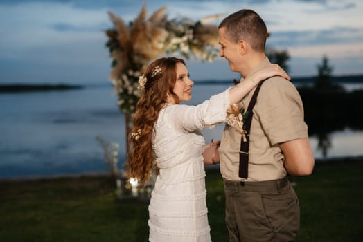 the first wedding dance of the bride and groom in the glade of the country club in the light of sunset and warm garlands