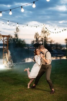 the first wedding dance of the bride and groom in the glade of the country club in the light of sunset and warm garlands
