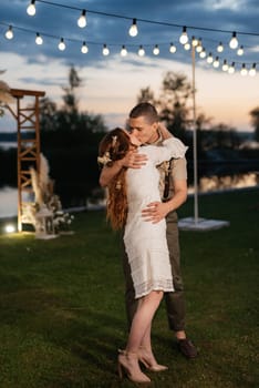 the first wedding dance of the bride and groom in the glade of the country club in the light of sunset and warm garlands