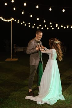 the first wedding dance of the bride and groom in the glade of the country club in the light of sunset and warm garlands