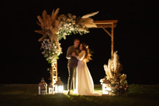 bride and groom against the backdrop of an evening wedding arch with warm live fire