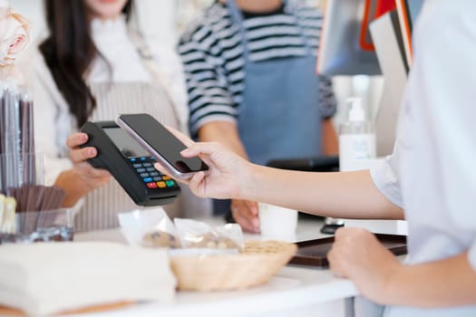 Female customer holding phone near nfc terminal make contactless mobile payment with waitress barista saleswoman on coffeeshop counter, woman client pay in cafe with cellphone via pos machine. Tap-to-pay technology is so convenient.
