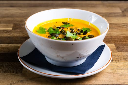 Pumpkin and carrot soup with cream and parsley on a dark wooden background