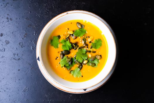 Pumpkin and carrot soup with cream and parsley on a dark wooden background