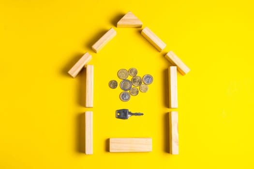 Wooden house model with coins, key, money, copy space on yellow background.