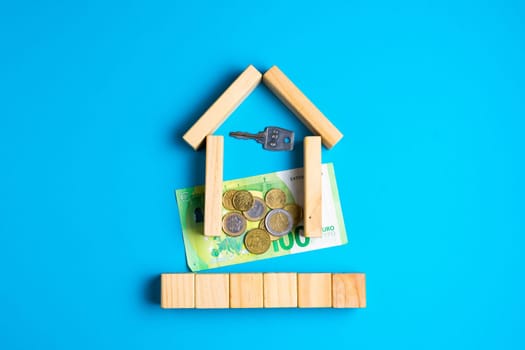 Wooden house model with coins, key, money, copy space on blue background.