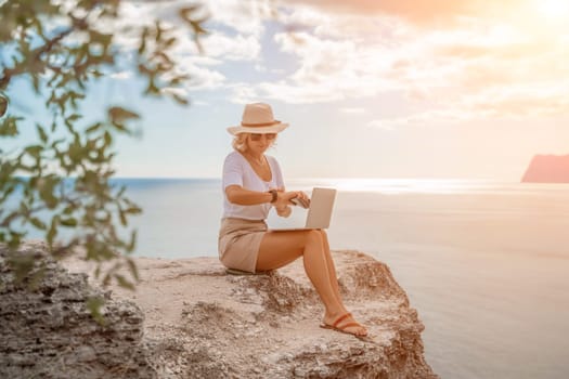 Freelance women sea working on the computer. Good looking middle aged woman typing on a laptop keyboard outdoors with a beautiful sea view. The concept of remote work